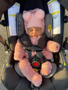 a baby sleeping in a car seat wearing a pink teddy bear hat and safety harness