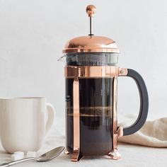 a french press coffee maker sitting next to a cup and saucer on a table