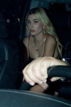 a woman sitting in the back seat of a car with her hand on the steering wheel