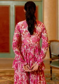 a woman standing in front of a doorway wearing a pink dress with flowers on it