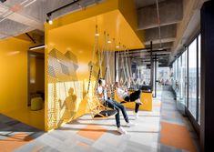 two people sitting on swings in the middle of an open room with yellow walls and flooring