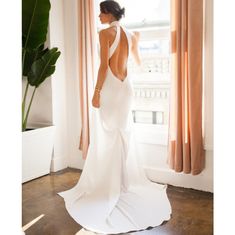 a woman standing in front of a window with her back turned to the camera and wearing a white dress