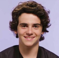 a young man with curly hair smiling at the camera