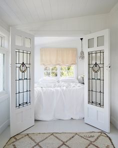 a bedroom with white walls and flooring has a bed in the corner, two doors leading to another room