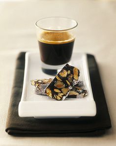 a white plate topped with pieces of cake next to a cup of coffee on top of a table