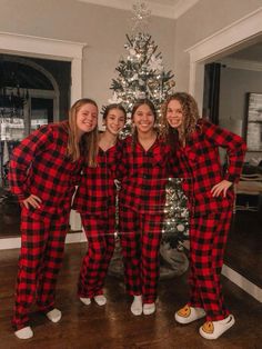 four women in matching pajamas standing next to a christmas tree