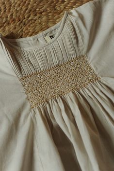 a close up of a white dress on a bed with a straw headboard in the background