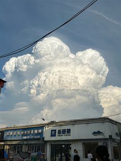 a large cloud is in the sky above a building with people standing outside it and some power lines