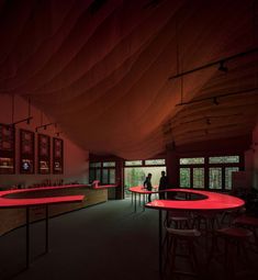 a person standing at a bar with red lights on the ceiling and tables in front of them