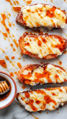 four pieces of bread covered in cheese and sauce next to a small bowl of honey