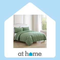 a green comforter and pillows on a bed in front of a window with the words at home above it