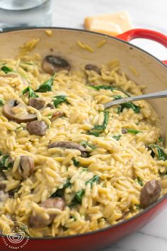 a red pan filled with pasta and mushrooms on top of a white marble countertop