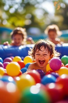 two children playing in a ball pit with one child laughing and the other looking at the camera