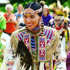 a native american woman with feathers on her head and other people in costume behind her