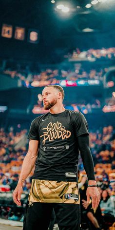 a man standing on top of a basketball court wearing a black shirt and gold shorts