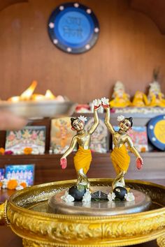 two figurines are standing on top of a gold tray in front of a wall