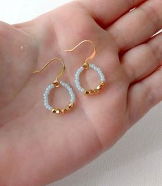 a hand holding two pairs of gold and white beaded earrings on it's palm