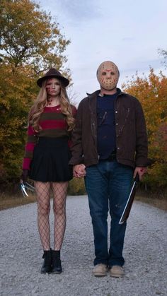 a man and woman dressed up as zombies walking down a dirt road with trees in the background