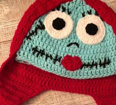 a crocheted hat with googly eyes and mouth is laying on a wooden surface