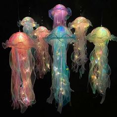 three jellyfish lights hanging from strings in the dark, one is multicolored