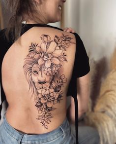 a woman with a lion tattoo on her back and flowers in her hair is looking at the camera