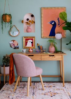 a pink chair sitting in front of a desk with pictures on the wall behind it