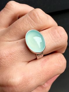 "A beautiful bright aqua blue oval chalcedony. This chalcedony is AAA quality and 100% natural. The stone has been set in sterling silver and a sterling silver bezel. The ring band is handmade from a sterling silver band with a unique pattern and is about 1/4\" wide or 6mm wide. Please note the width and thickness of the ring band and adjust your ring size as needed! The ring's total height is just over a 1/4\" and it is 13mm x 18mm in size. This stone is a light blue but certain light can bring Oval Turquoise Moonstone Ring, Turquoise Chalcedony Gemstone Rings, Turquoise Oval Moonstone Ring For Anniversary, Oval Chrysoprase Opal Ring For Gift, Spring Fashion Chic, Silver Jewlery, Christian Bracelets, Chalcedony Stone, Chalcedony Ring