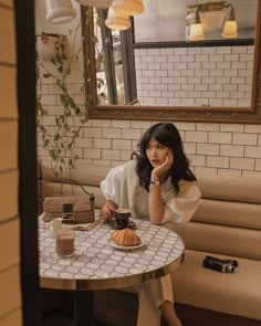 a woman sitting at a table with a cup of coffee and croissant in front of her