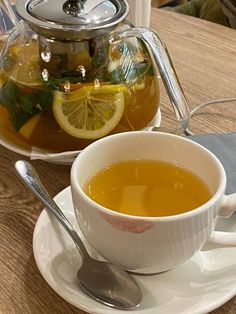 a cup of tea with lemon slices on the side and a tea pot in the background