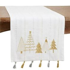 a white table runner with gold christmas trees on it and tassels hanging from the edge