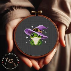 a person holding a cross - stitch pattern with a purple witch hat on their head