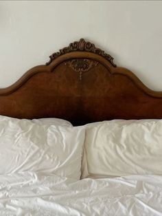 an old wooden headboard with white sheets and pillows