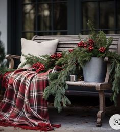 a wooden bench covered in christmas greenery next to a plaid blanket and throw pillow