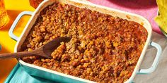 a casserole dish filled with chili and beans on a blue towel next to bread