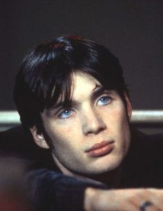 a close up of a person wearing a black shirt and blue eyes with one hand on his chest