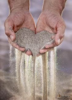 two hands holding sand in the shape of a heart