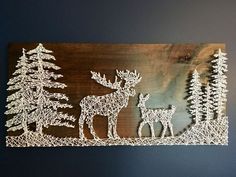 a string art piece depicting two deer in the woods with pine trees on each side