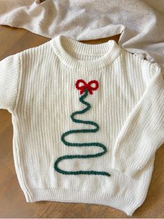 a white sweater with a red bow on the front and green ribbon on the back