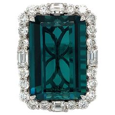 This exquisite ring features a 21.33-carat octagonal Indicolite Tourmaline as the centerpiece, surrounded by a dazzling halo of 2.56 carats of white round and baguette diamonds. The ring is meticulously handcrafted with a classic four-prong setting and a three-stripe pave diamond band, all set in 18K white gold. The clarity of the center stone is highlighted by the gallery design, which is visible in the images. All gemstones and diamonds are ethically sourced. Please note that the images have b Luxury White Gemstones With Accents, Luxury Round Cut Gemstone Jewelry, Luxury Round Jewelry With Center Stone, Luxury White Gold Crystal Ring With Round Stone, Luxury Classic Rings With Gemstone Accents, Luxury White Gold Crystal Ring With Accent Stones, Luxury Classic Crystal Ring With Accent Stones, Luxury Classic Diamond Gemstones, Luxury Carved Round Jewelry