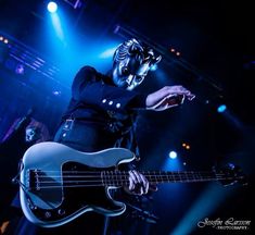 a man playing a bass on stage with blue lights behind him and his face painted like a skeleton