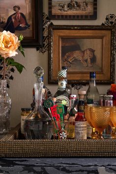 an assortment of liquor bottles and glasses on a table with a painting in the background