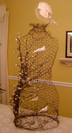 a wire mannequin sitting on top of a table covered in branches and white flowers