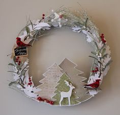 a christmas wreath made out of paper with reindeer and pine trees on the front, surrounded by holly