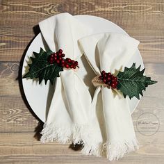 a white plate topped with two napkins covered in holly and red berries on top of a wooden table