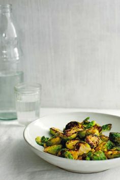 a white bowl filled with brussel sprouts next to a glass of water