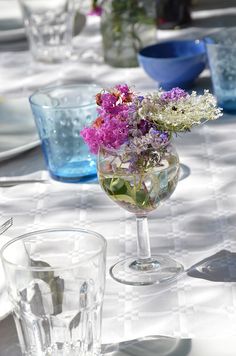 the table is set with glasses, plates and vases filled with flowers on it