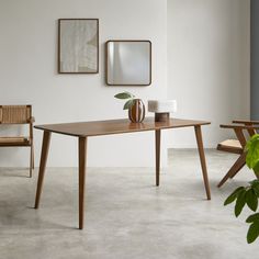 a wooden table sitting next to two chairs and a plant in a vase on top of it