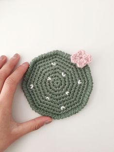 a hand holding a crocheted potholder with a flower on it's side