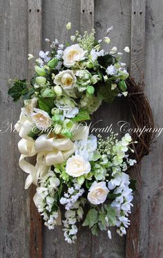 a wreath with white flowers and greenery hanging on a wooden fence