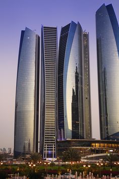 the tall buildings are next to each other in front of some water fountains and trees